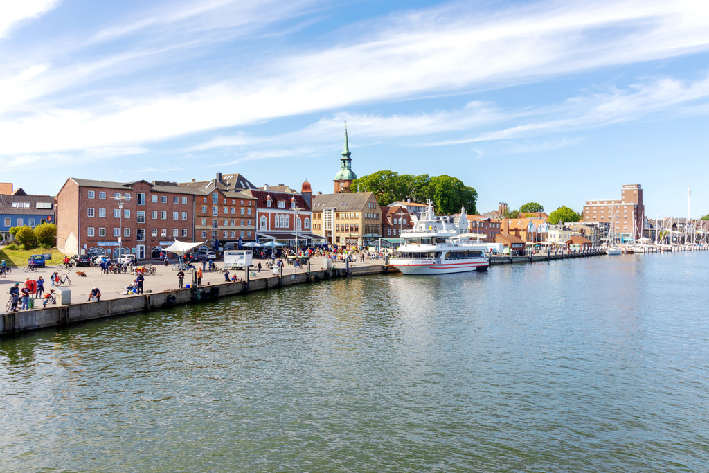 Wandbild: Hafen in Kappeln | Dieses Wandbild im Querformat zeigt den Hafen in Kappeln im Frühling. Die Fähre liegt im Hafen und spiegelt sich leicht im Wasser der Schlei. Am Himmel befinden sich zahlreiche Schleierwolken.  - Realisiert mit Pictrs.com