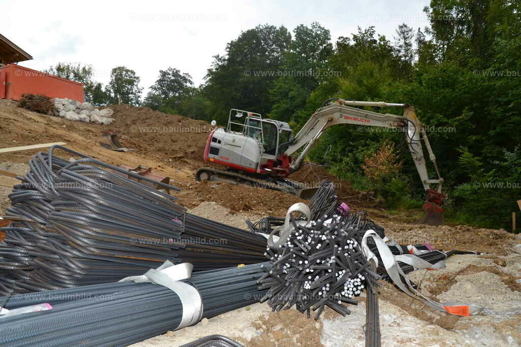 Bewehrung für Fundamente | Gebogener Baustahl für Fundamentbewehrung, dahinter Bagger bei Erdarbeiten
