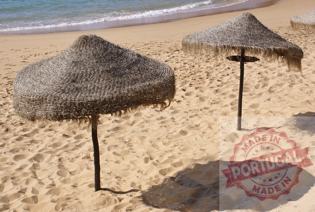 Tiki umbrellas providing shade on sandy beach | Two tiki umbrellas stand on a sandy beach with ocean waves in the background - Realisiert mit Pictrs.com