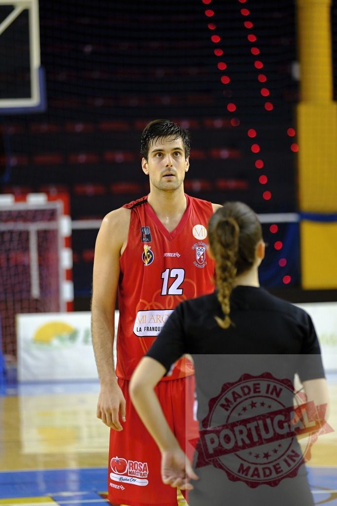 Basketball player standing on court facing female referee | Basketball player in red jersey looking directly ahead during a game in an indoor court - Realized with Pictrs.com