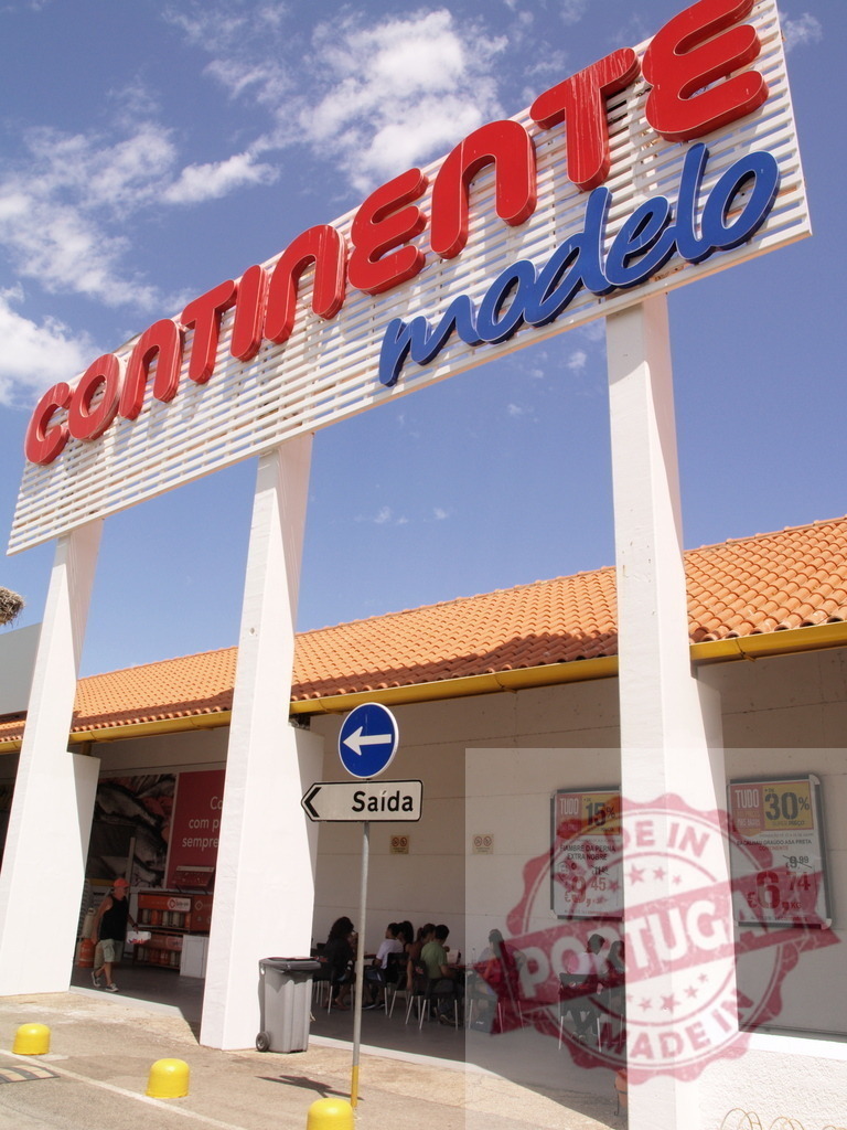 Continente Modelo supermarket sign against blue sky | Continente Modelo hypermarket entrance with a large outdoor sign and people relaxing - Realisiert mit Pictrs.com