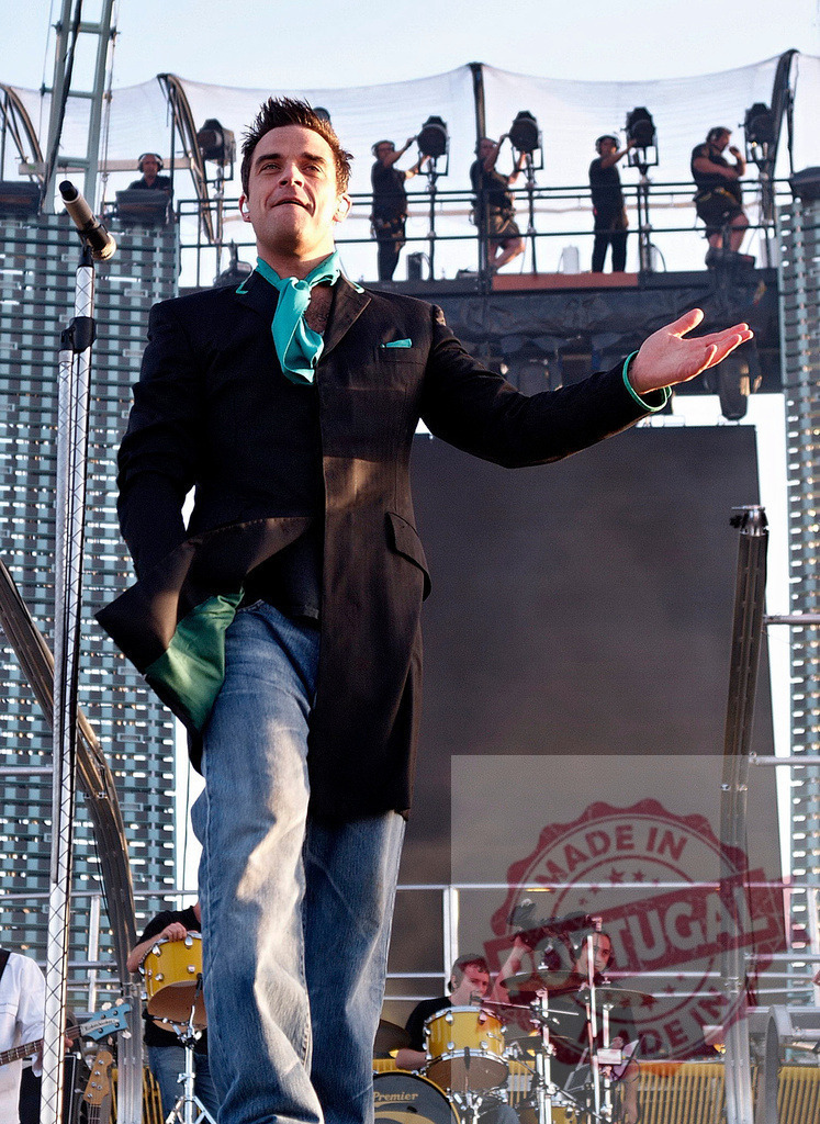 Robbie Williams performing on stage, interacting with audience during concert | Robbie Williams interacting with his audience during a live concert, wearing a suit and jeans - Realized with Pictrs.com