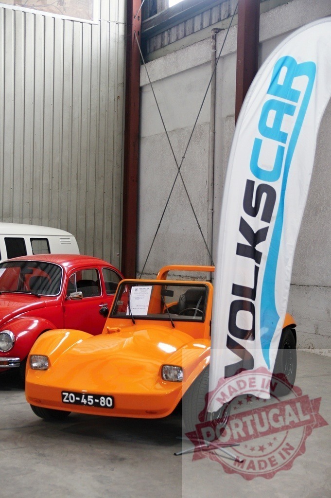 Orange VOLKSCAR Dune Buggy standing next to a red Volkswagen Beetle in a garage | Small orange VOLKSCAR dune buggy parked next to a red Volkswagen Beetle in a garage with a VOLKSCAR promotional banner - Realisiert mit Pictrs.com