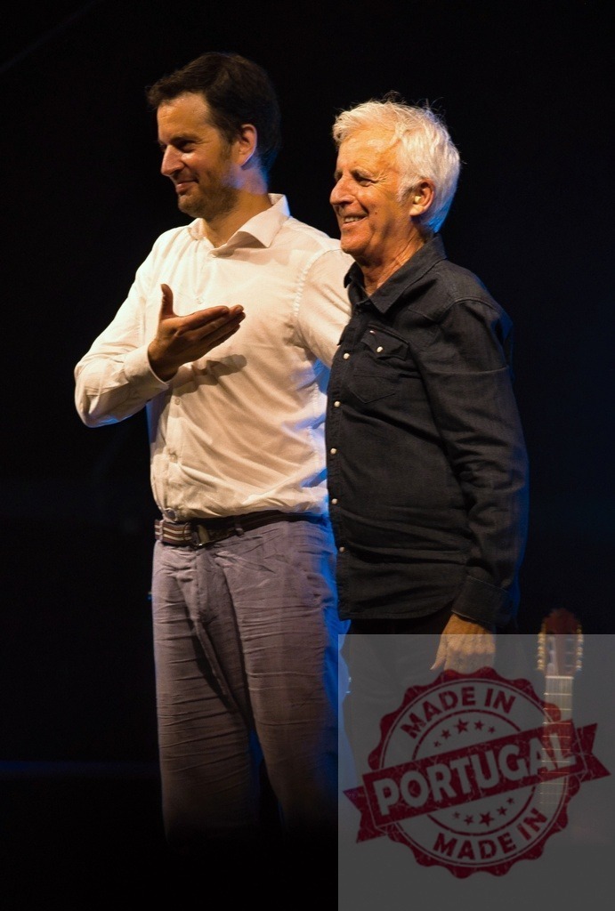 Graham Nash smiling with Manel Fuentes onstage during concert | Graham Nash and Manel Fuentes sharing a happy moment onstage during a performance - Realized with Pictrs.com