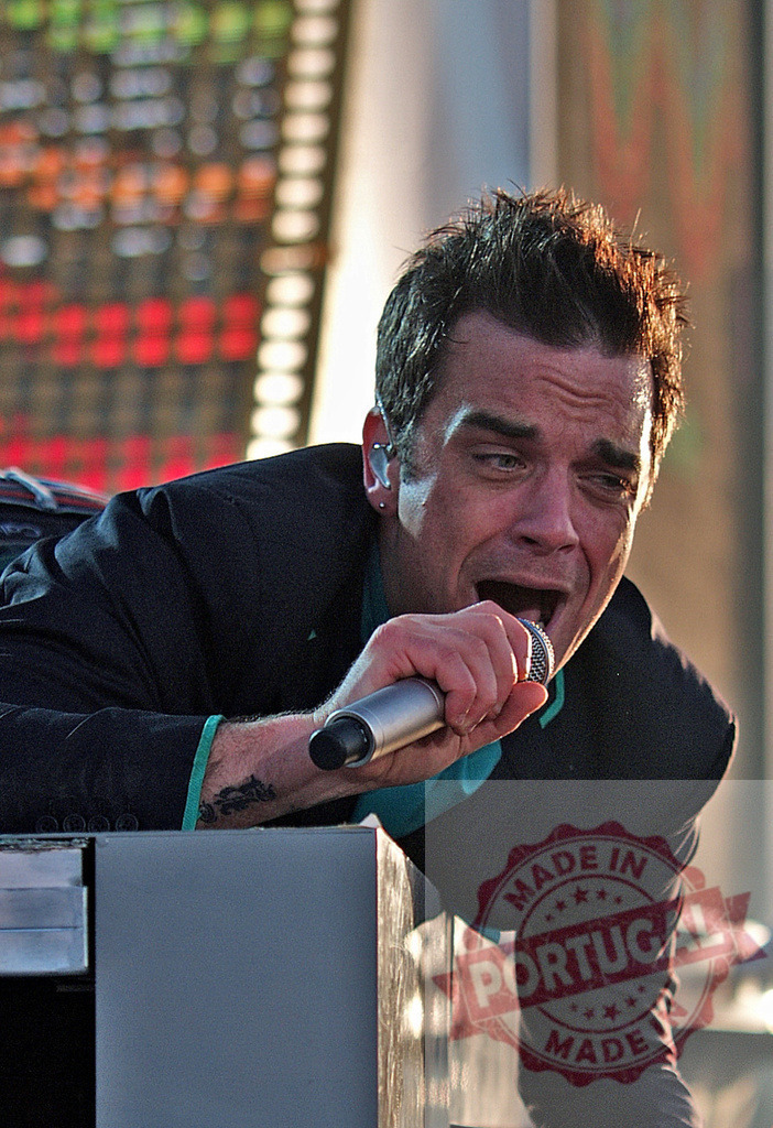 Robbie Williams singing with microphone during live concert | Singer Robbie Williams passionately performing live on stage, engaging with audience - Realized with Pictrs.com