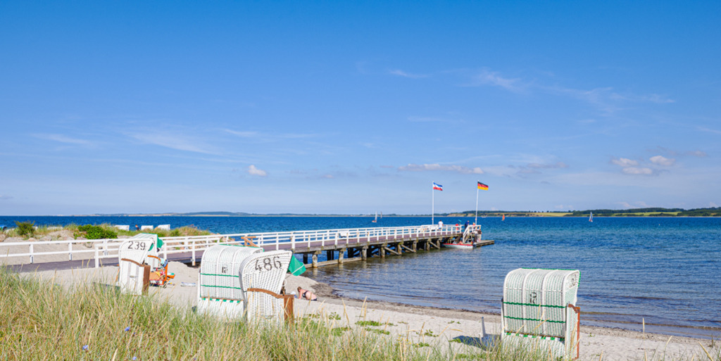 Strand in Hohwacht | Sommer an einem Badestrand in Hohwacht an der schleswig-holsteinischen Ostseeküste. Die Seebrücke und die Strandkörbe erzeugen ein inniges Gefühl von Wärme, Urlaub, Entspannung an der wunderbaren See. — Auflösung des Originals: 6016 x 3008 px. - Realisiert mit Pictrs.com
