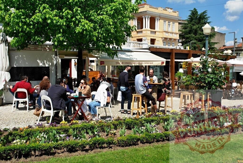 People relaxing at outdoor cafe in city square during sunny day. Portugal - Norte | People enjoying drinks and conversation on an outdoor cafe terrace, surrounded by blooming flowers - Realisiert mit Pictrs.com