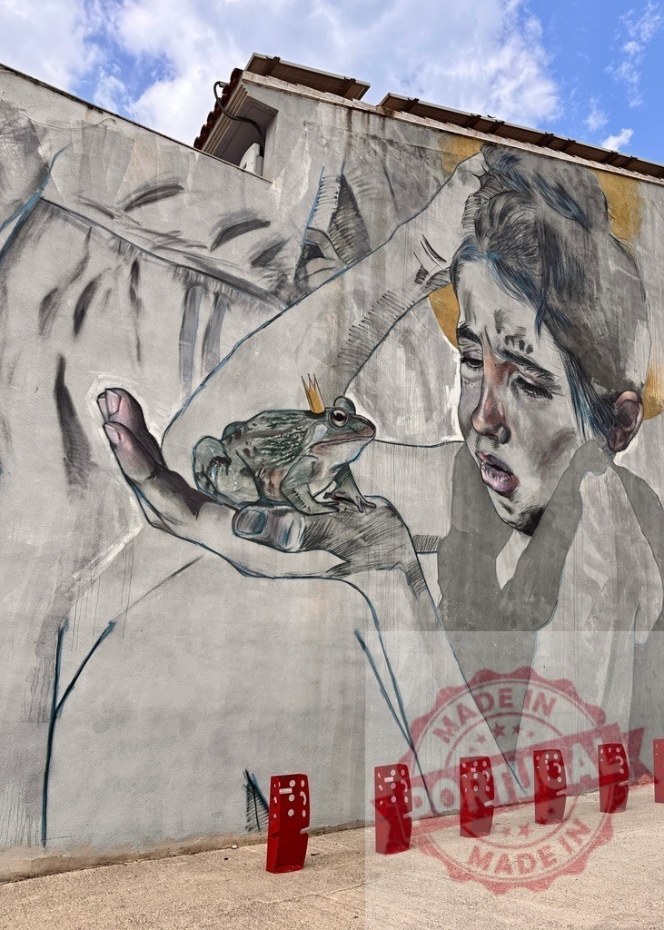 Girl holding frog prince mural on urban wall | Street art mural depicting a girl holding a frog with a crown, suggesting a fairy tale - Realized with Pictrs.com