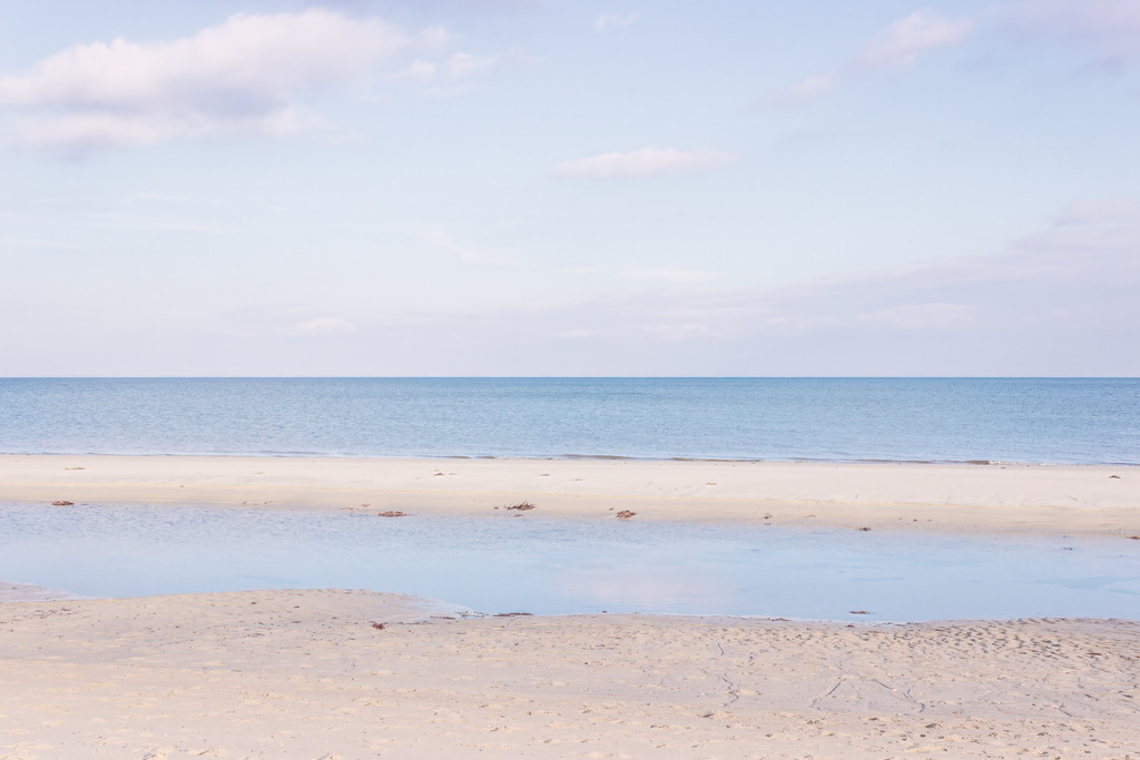 Küstenruhe am Morgen – Weite unter hellem Himmel | Dieses Motiv zeigt die stille Küstenlandschaft im weichen Licht des beginnenden Tages. Der Strand, das flache Wasser und das ruhige Meer gehen harmonisch ineinander über und erzeugen eine klare, minimalistische Weite. Das sanfte Morgenlicht legt einen warmen Schimmer auf die Szene und lässt Himmel und Wasser in zarten Farbtönen miteinander verschmelzen. Die Komposition vermittelt Ruhe, Gelassenheit und die natürliche Schönheit eines stillen Moments am Meer. Als Wandbild erhältlich auf Acrylglas und weiteren hochwertigen Materialien.