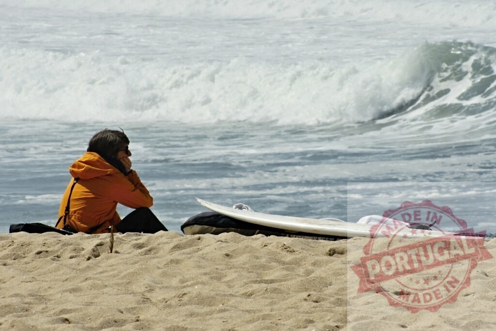 Surfer sitting on beach contemplatively watching ocean waves | Surfer sitting on sand watching ocean waves, experiencing solitude and waiting for ideal conditions - Realized with Pictrs.com