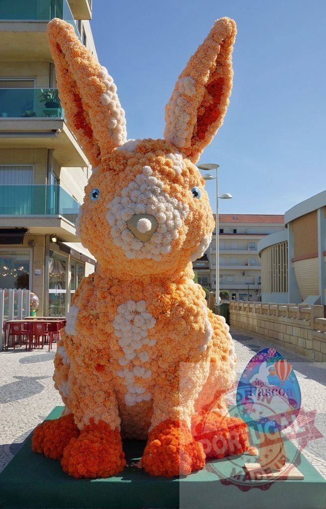 Giant floral Easter bunny sculpture in a city street | Large orange and white bunny sculpture made of flowers for Easter celebration - Realisiert mit Pictrs.com