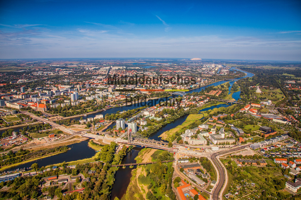 Magdeburg Luftbild neue Pylonstrombrücke Elbe Werder Heumarkt-6838 | Die Luftaufnahme zeigt große Teile Magdeburgs mit der Elbe, der Alten Elbe und der historischen Innenstadt in einem einzigen Panorama. Im Vordergrund prägen der Heumarkt und die Kaiser-Otto-Brücke das Stadtbild, während sich der Blick über die Altstadt bis zum Neustädter See erstreckt. Am Horizont ist bei klarer Sicht sogar die Kalihalde bei Zielitz – der „Kalimandscharo“ – zu erkennen. Das Panorama vermittelt die räumlichen Zusammenhänge der Landeshauptstadt und verdeutlicht die prägende Rolle der Elbe für die Entwicklung Magdeburgs. - Realisiert mit Pictrs.com