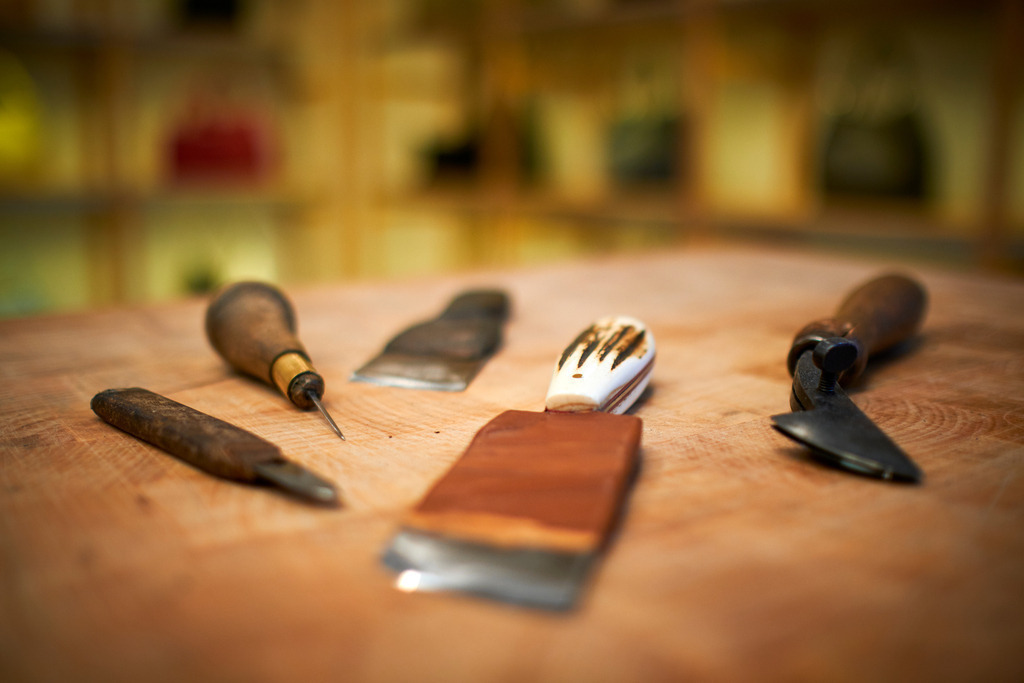 Albert Pattermann Wien | WIen, Austria - February 28, 2020; Albert Pattermann Wien; diverse Werkzeuge für die Lederbearbeitung auf einem Holztisch, im Hintergrund die Taschen. - Realisiert mit Pictrs.com