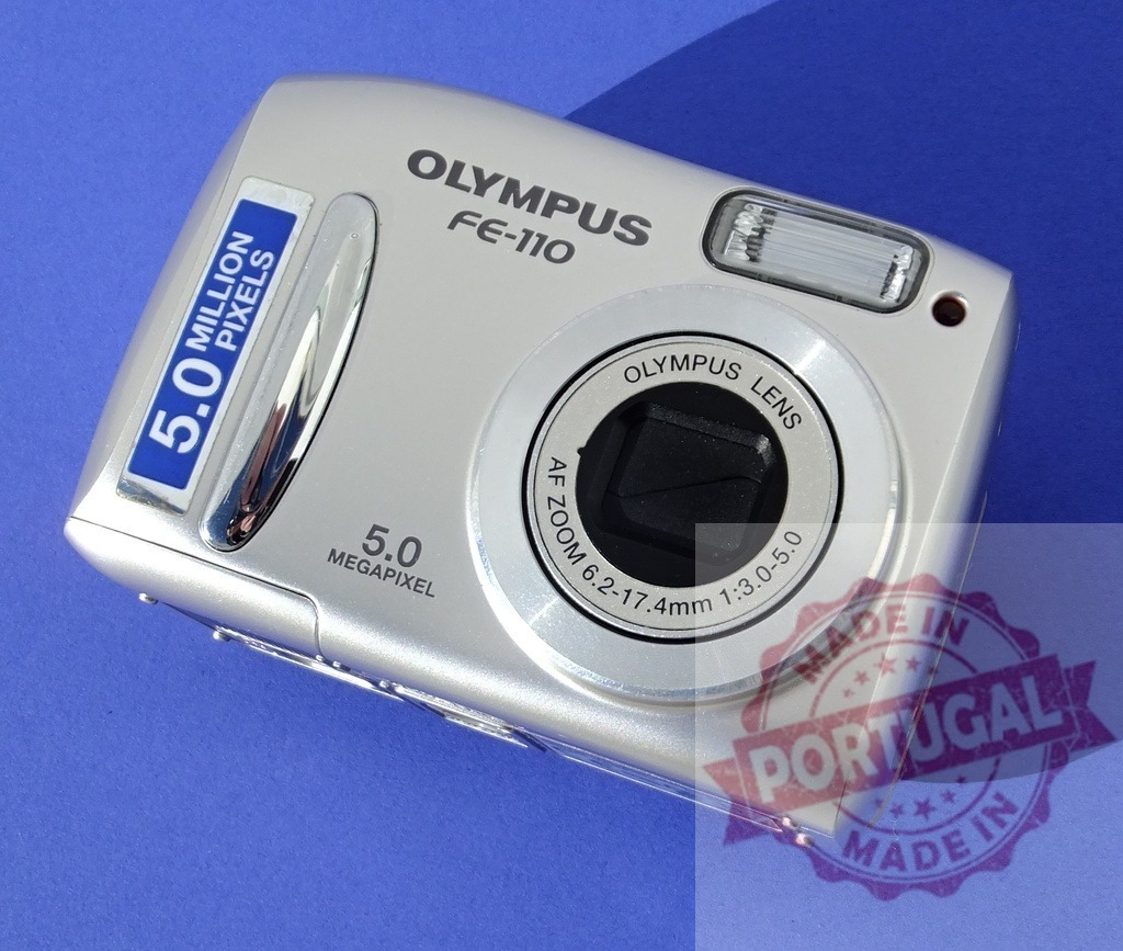 Olympus FE-110 compact digital camera on blue background | Silver 5.0 megapixel Olympus FE-110 point and shoot digital camera - Realized with Pictrs.com