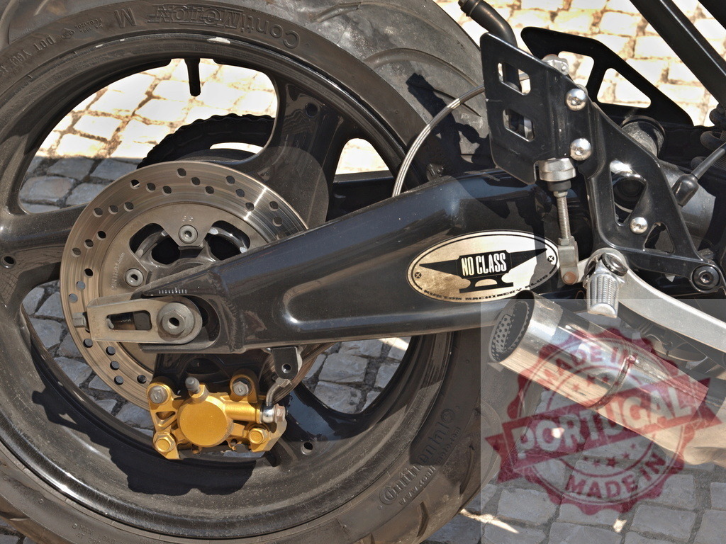 Motorcycle rear wheel showing disc brake and custom exhaust | Close-up of motorcycle rear wheel and mechanical parts on a cobblestone street - Realisiert mit Pictrs.com