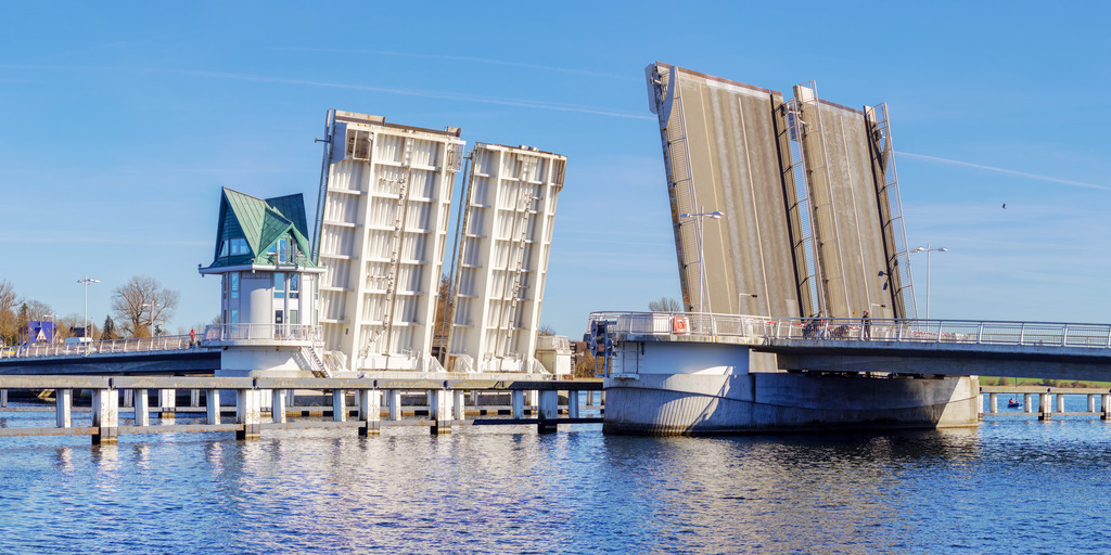 Panorama Wandbild: Schleibrücke in Kappeln | Kappeln – eine malerische Stadt an der Ostsee, die für ihre maritime Atmosphäre und idyllische Lage bekannt ist. Dieses Panorama-Wandbild fängt die beeindruckende Klappbrücke ein, die sich elegant über die Schlei erstreckt und das historische Flair der Region widerspiegelt. Der klare Himmel, die sanften Reflexionen im Wasser und die architektonische Schönheit der geöffneten Brücke verleihen dem Bild eine faszinierende Harmonie. Ideal für Wohnräume, Büros oder gemütliche Rückzugsorte – ein Stück norddeutsche Küstenlandschaft für dein Zuhause! - Realisiert mit Pictrs.com