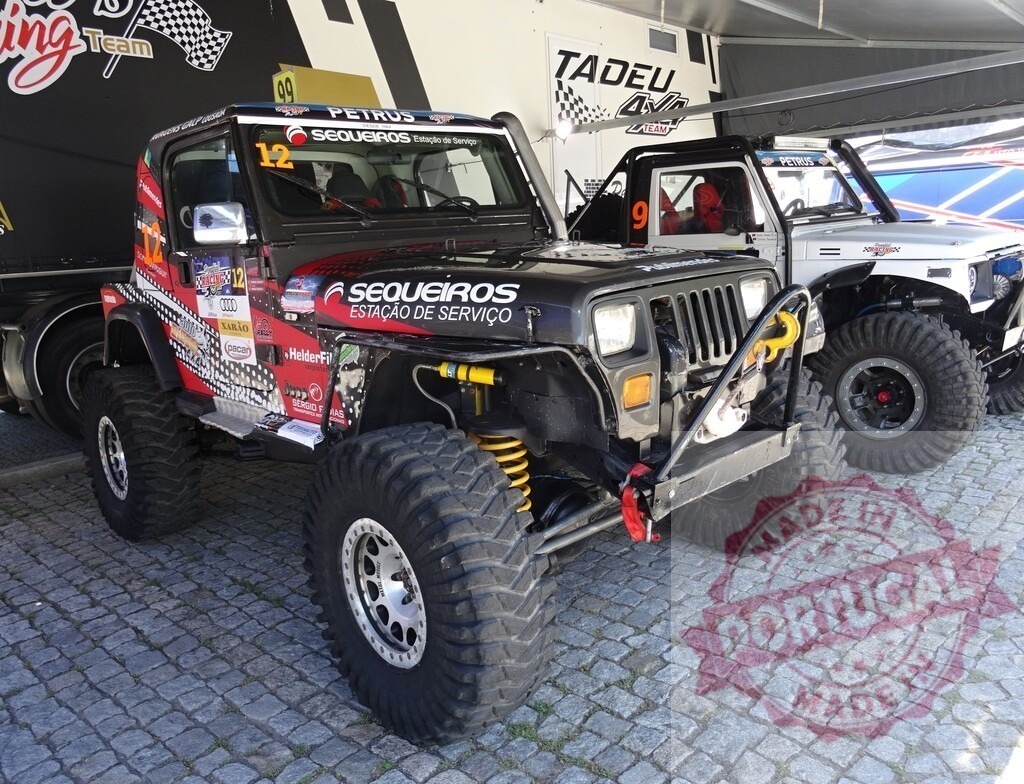 Customized Jeep Wrangler parked near a trailer, ready for an off-road competition | Tuned jeep wrangler with big tires parked near a trailer during an off-road competition - Realized with Pictrs.com