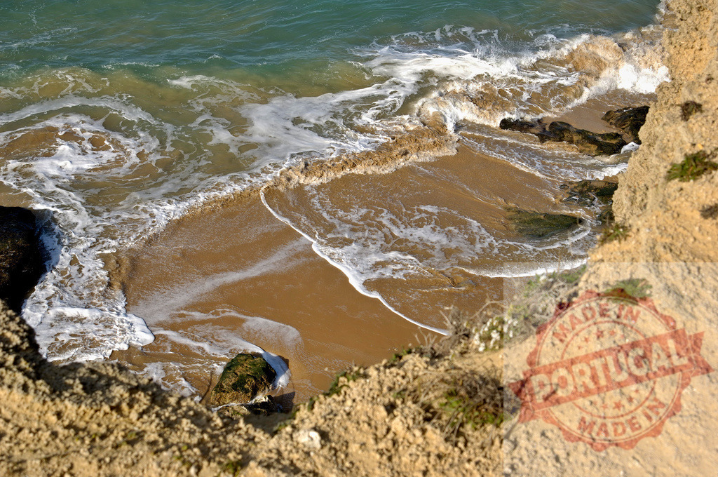 Ocean waves washing shore at base of cliff. Espana - Cadiz | Ocean waves breaking on a sandy beach at the base of a tall coastal cliff - Realized with Pictrs.com