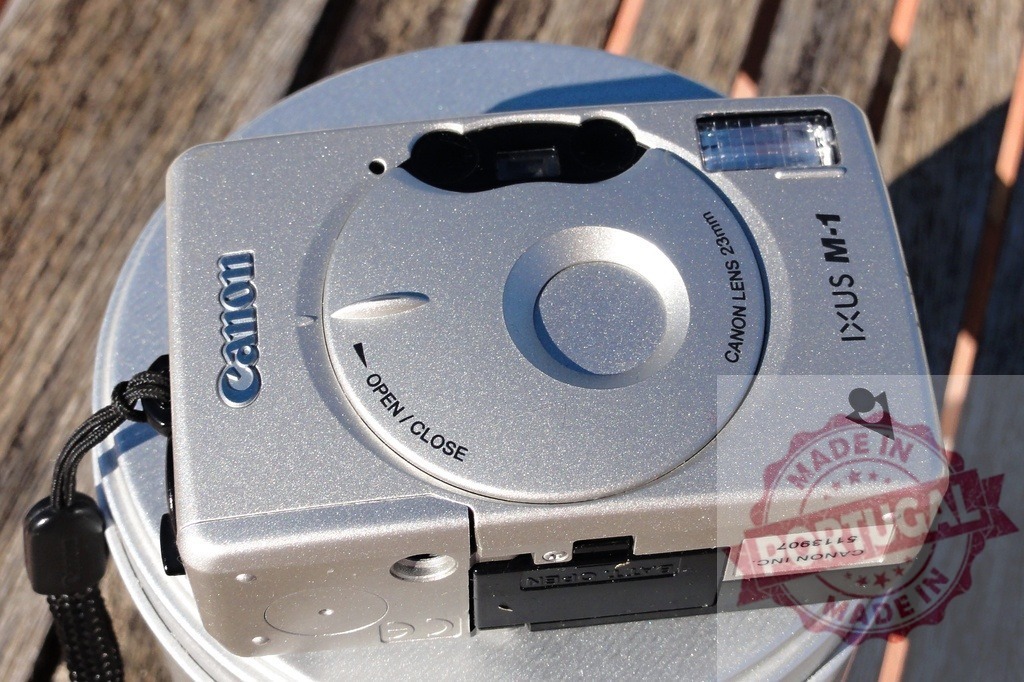 Canon IXUS M-1 APS film camera close-up | Silver Canon IXUS M-1 APS film camera sitting outdoors in directional sunlight - Realisiert mit Pictrs.com