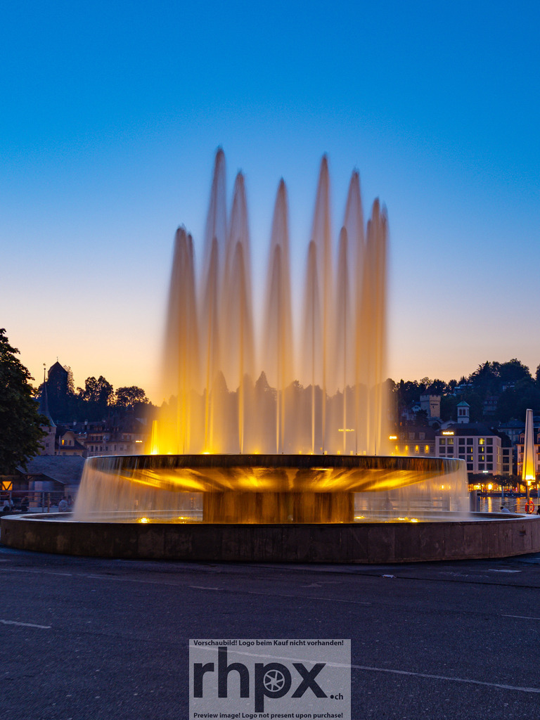 Wagenbach-Brunnen am KKL | Wasser. Licht. Eleganz.
Die illuminierten Wasserfontänen des Wagenbach-Brunnens steigen vor der modernen Kulisse des KKL in den Abendhimmel empor. Die goldene Beleuchtung kontrastiert sanft mit dem kühlen Blau der Dämmerung und schafft eine fast meditative Dynamik.
Wähle unter "Produktauswahl" dein Wunschformat: Vom klassischen Wandbild über Puzzle &amp; Tassen bis zum digitalen Download (z.B. als Handy-Hintergrund).
 - Realisiert mit Pictrs.com
