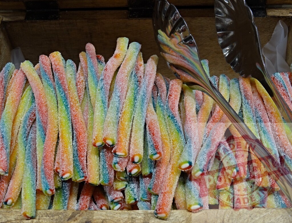 Colorful sour gummy candy worms in wooden crate | Vibrant rainbow-colored sour gummy worms displaying sweet and tangy sugar coating - Realisiert mit Pictrs.com