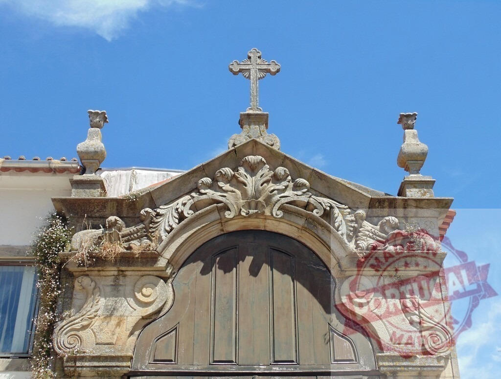 Stone church facade with ornate religious cross carving. Aveiro - Portugal | Stone church facade featuring ornate baroque carvings, a prominent christian cross, and an arched wooden door - Realisiert mit Pictrs.com