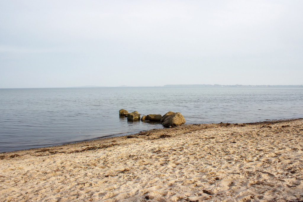 Wandbild: Strand in Ohrfeldhaff | Dieses Wandbild im Querformat zeigt den Sandstrand in Ohrfeldhaff im Herbst. Ins Wasser ragt eine kleine Steinmole.  - Realisiert mit Pictrs.com