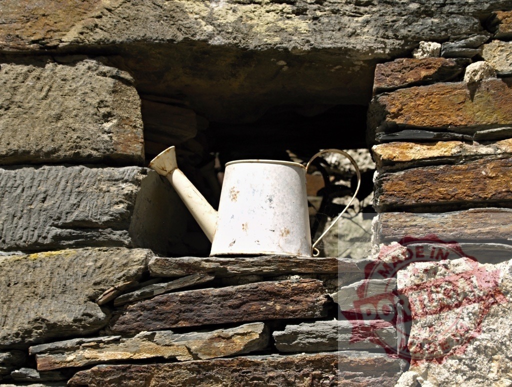 Vintage watering can sitting in stone wall niche | Old watering can resting in a textured stone wall opening on a sunny day - Realisiert mit Pictrs.com