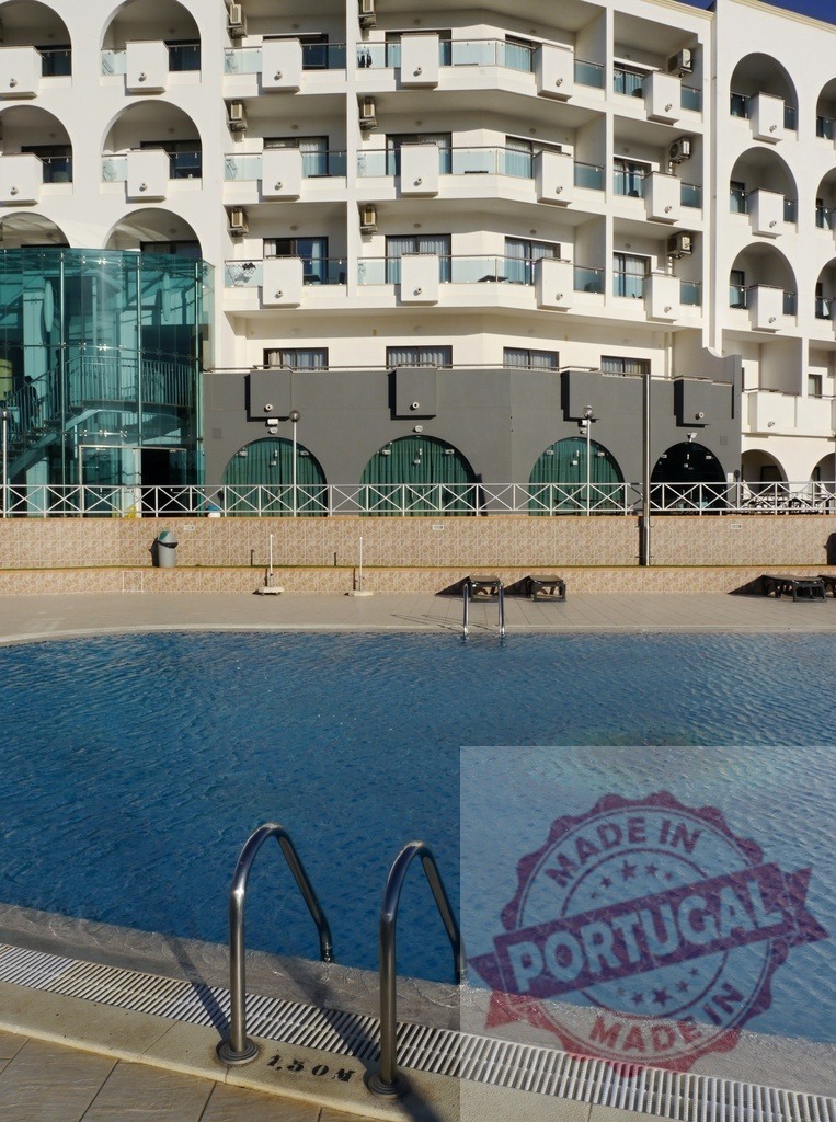 Hotel swimming pool with modern facade on a sunny day | Open-air hotel swimming pool reflecting a modern building under blue sky - Realisiert mit Pictrs.com