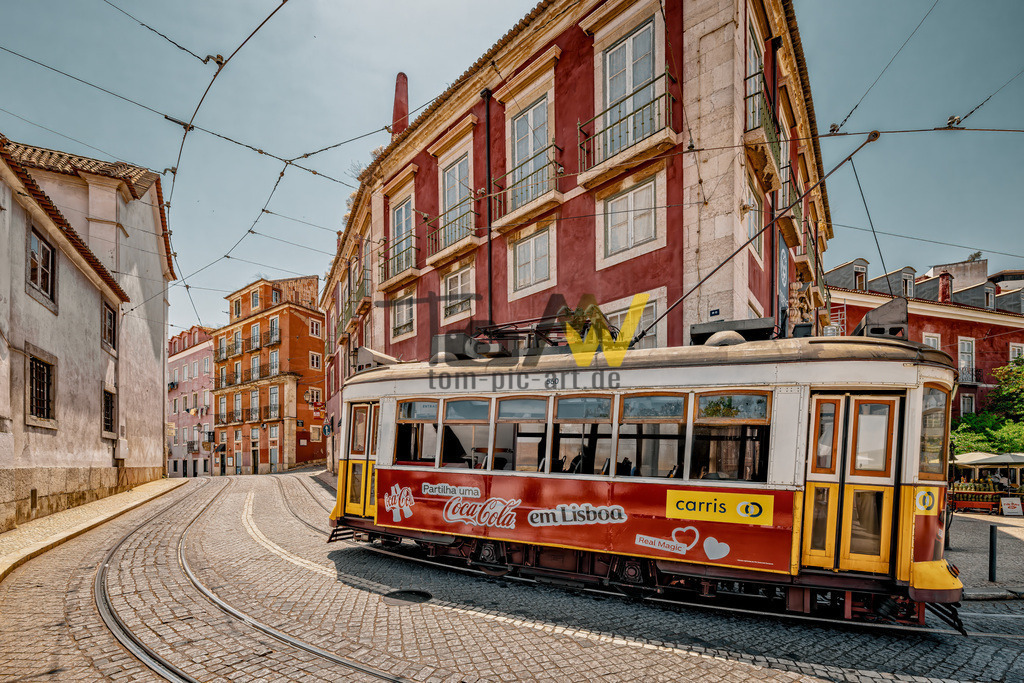 Eine historische Straßenbahn in der Altstadt von Lissabon | Das Bild zeigt eine der berühmten historischen Straßenbahnen (Elétrico) in Lissabon, Portugal, die durch die engen, gepflasterten Straßen der Stadt fährt. Diese Art von Straßenbahnen, insbesondere die der Linie 28E, sind eine beliebte Touristenattraktion und ein wichtiges öffentliches Verkehrsmittel. Die Linie 28E verbindet den Martim Moniz-Platz mit dem Stadtteil Prazeres und passiert dabei zahlreiche Sehenswürdigkeiten. - Realisiert mit Pictrs.com