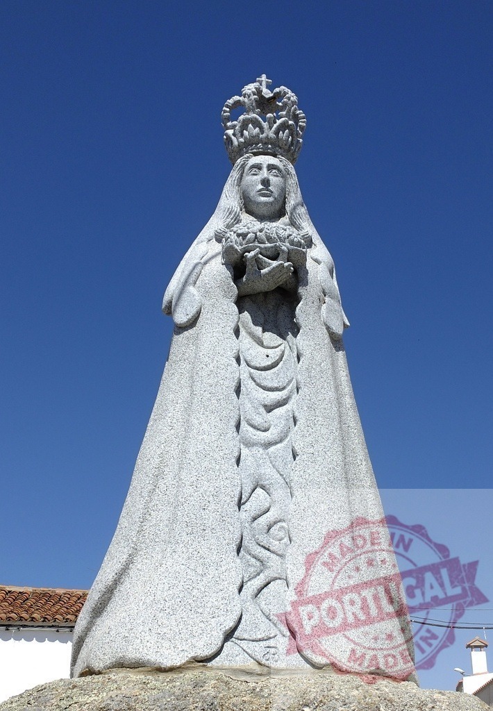 Virgin Mary granite sculpture with crown against blue sky. Spain - Extremadura | Religious granite sculpture depicting Virgin Mary wearing a crown and holding flowers under clear sky - Realized with Pictrs.com