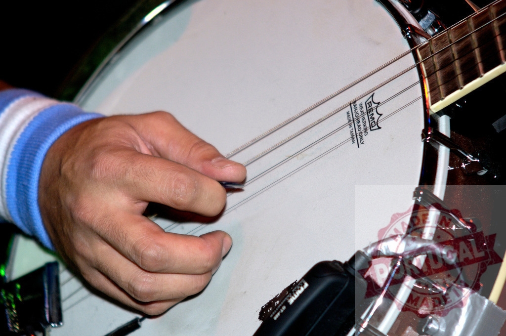 Musician playing banjo with pick during live performance | Close-up of a musician's hand plucking the strings of a banjo with a pick during a live musical performance - Realisiert mit Pictrs.com