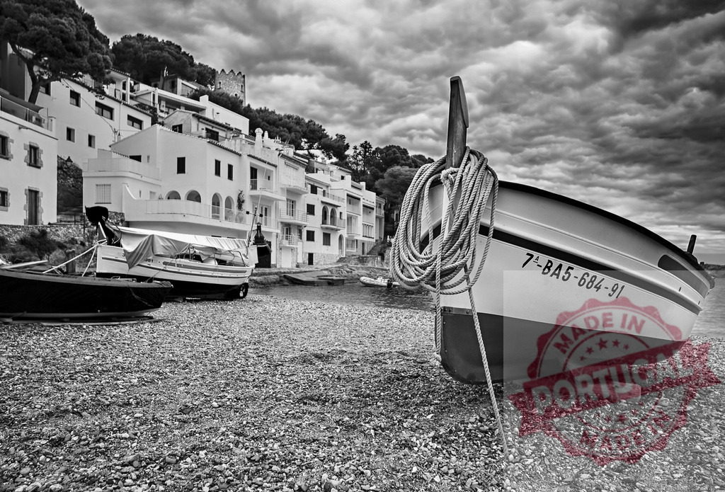 Fishing boat resting on the beach of Cadaqués with dramatic sky | Black and white photography of a fishing boat resting on the beach of the coastal village of Cadaqués, with a dramatic cloudy sky - Realized with Pictrs.com