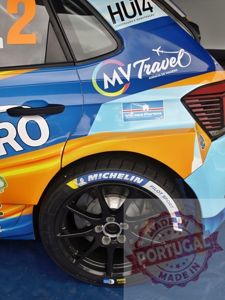 Rally car side view showing wheel and sponsor logos | Rally car side displaying Michelin tire, colorful livery, and sponsor advertisements - Realisiert mit Pictrs.com