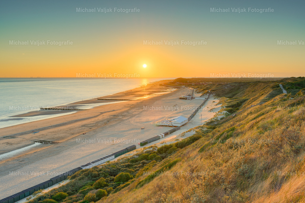 Abends in den Dünen bei Zoutelande | Von den Dünen eröffnet sich ein stimmungsvoller Blick über den weitläufigen Strand von Zoutelande und die Nordsee. Die tief stehende Sonne taucht den Himmel und die Küstenlandschaft in warme, goldene Farbtöne und lässt den Tag an der zeeländischen Küste langsam ausklingen.Die Dünen im Vordergrund verleihen dem Bild Tiefe, während der geschwungene Strand und das Meer den Blick bis zum Horizont führen. Das sanfte Licht des Sonnenuntergangs schafft eine ruhige und besonders atmosphärische Stimmung.Ein stimmungsvolles Landschaftsfoto von Zoutelande in Zeeland, Niederlande, das die besondere Schönheit eines Sonnenuntergangs an der niederländischen Nordseeküste einfängt. - Realisiert mit Pictrs.com