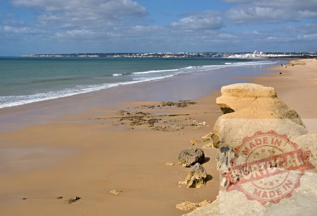 Praia da Rocha beach and ocean coastline | Empty sandy beach with rock formations, ocean waves, and a distant town - Realized with Pictrs.com