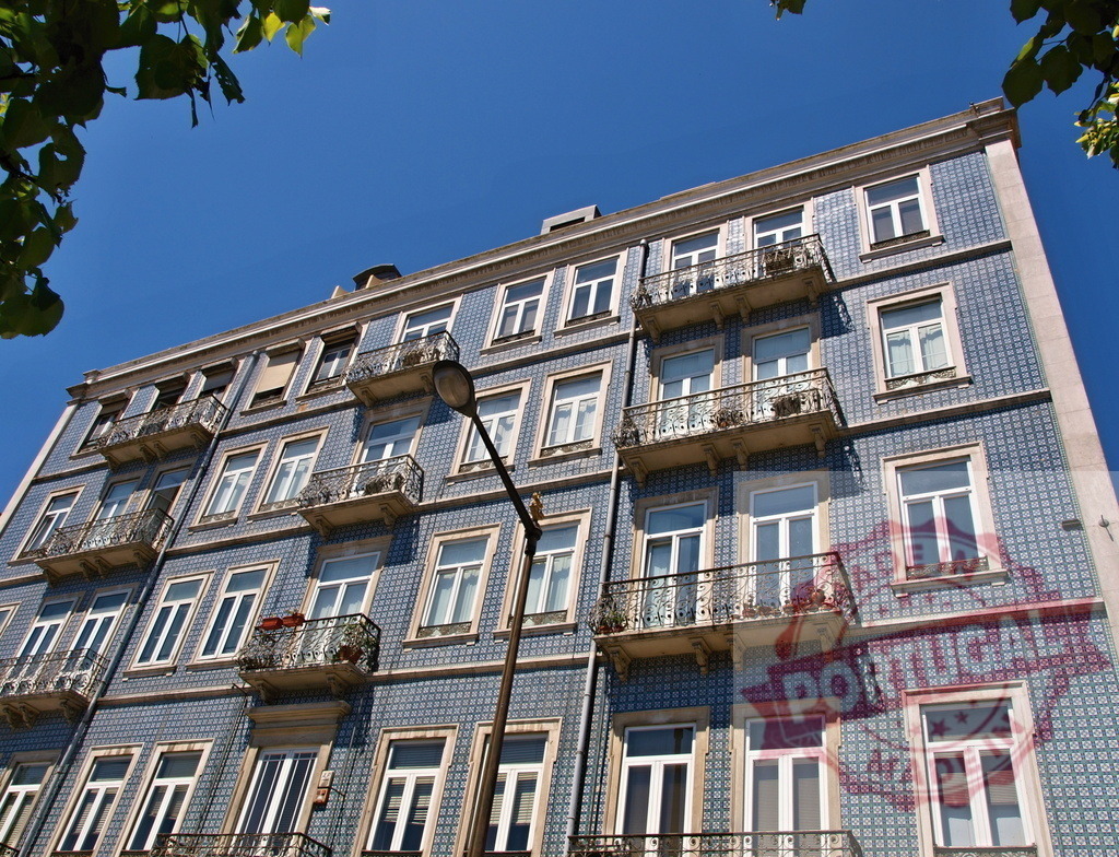 Lisbon building facade featuring azulejo tiles and balconies | Building facade tiled with traditional blue azulejo, balconies, and windows under a clear sky - Realized with Pictrs.com
