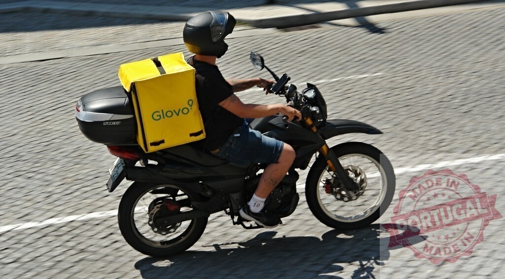 Urban Glovo courier delivering food on motorcycle along city street | Glovo motorbike courier rides down a sunny city road for a fast food delivery - Realisiert mit Pictrs.com