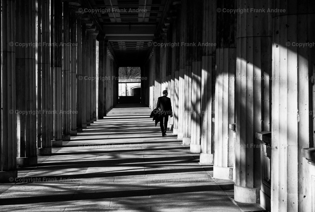 Entspannt | Ein Mann geht mit Mantel in der Hand entspannt durch die Arkaden des Lustgartens in Berlin. Straßenfotografie aus Berlin in schwarz weiß. - Realisiert mit Pictrs.com