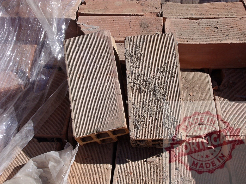 Two hollow bricks lying on top of a pile of bricks and plastic wrap | Two hollow bricks with striped surface lying on top of a pile of bricks and plastic wrap - Realized with Pictrs.com