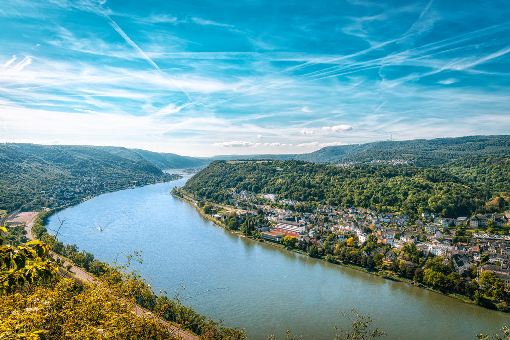 Panoramablick auf das malerische UNESCO-Welterbe Oberes Mittelrheintal | Das Bild zeigt den Blick von der Hindenburghöhe im UNESCO-Welterbe Oberes Mittelrheintal.Zu sehen ist der Rhein bei Flusskilometer 566.Ortschaften: Auf der rechten, vorderen Flussseite liegt die Gemeinde Filsen, während im Hintergrund auf der linken Seite die Stadt Boppard zu erkennen ist.Wanderwege: Direkt an diesem Aussichtspunkt verläuft der bekannte Premium-Fernwanderweg Rheinsteig - Realisiert mit Pictrs.com
