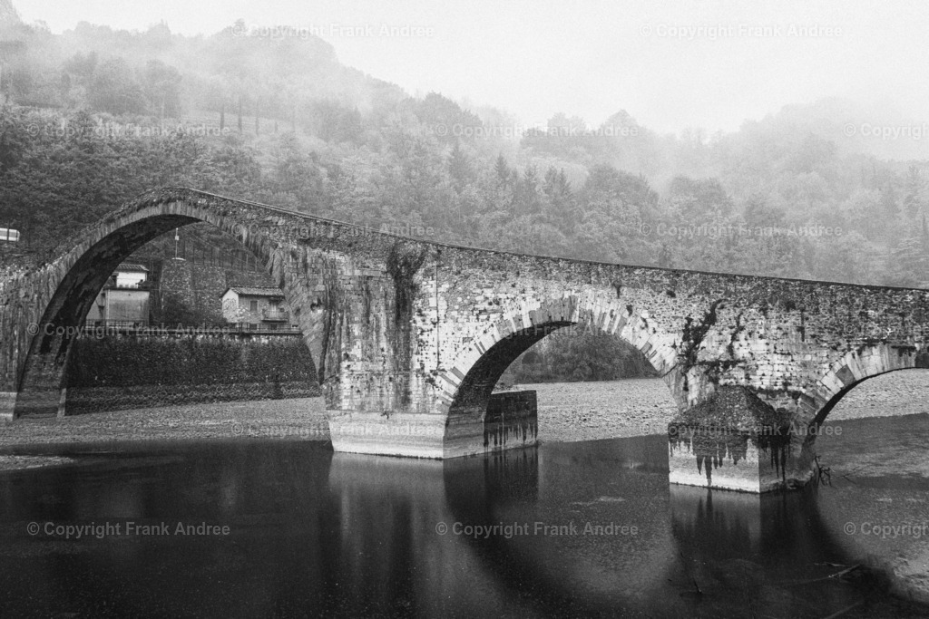 Ponte della Maddalena (Teufelsbrücke) Toskana | Schwarz weiß Fotografie der Teufelsbrücke Ponte della Maddalena an einem nebligen Tag in der Toskana. Seitliche Ansicht des imposanten Bauwerkes. Im Hintergrund die Berglandschaft durch die Nebel zieht. - Realisiert mit Pictrs.com