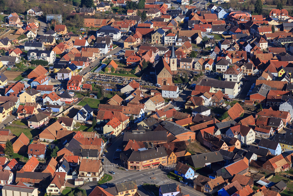 Aerial view: Town center from the west with Eglise Catholique and Cimetière communal den Mommenhim in Mommenheim in the state Bas-Rhin, France. – Photo: IMG_097614.jpg taken on 03/16/2017 by Werner Riehm/FLY-FOTO.com – Resolution of the original: 5472 x 3648 px