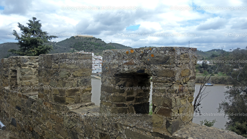 Blick von der Festungsmauer der Burg von Alcoutim nach Spanien | Castelo de Alcoutim (Neuere Burg): Die heutige Hauptsehenswürdigkeit im Ortskern wurde im 14. Jahrhundert (ca. 1304) unter König D. Dinis zum Schutz der Grenze gegenüber Spanien errichtet. Direkt am Fluss Guadiana, gegenüber der spanischen Burg von Sanlúcar de Guadiana. Im Inneren befindet sich ein archäologisches Museum, das unter anderem eine beeindruckende Sammlung von Brettspielen aus der islamischen Zeit ausstellt. Sie diente jahrhundertelang der Überwachung des Schiffsverkehrs auf dem Fluss. Alcoutim ist eine Kleinstadt und ein Kreis mit 2523 Einwohnern in Portugal, im Distrikt Faro. Sie liegt im äußersten Nordosten der Algarve am hier zu sehenden Grenzfluss Guadiana. Auf der anderen Seite liegt Spanien. - Realisiert mit Pictrs.com