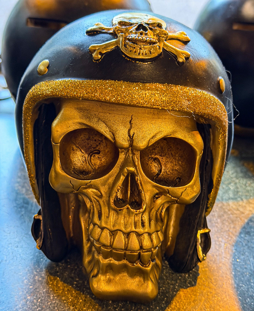 Goldener Biker Totenkopf – Rustikale Rocker Fotokunst Wandbild | Charakterstarke und detailreiche Fotokunst: Dieses High-End Wandbild zeigt eine faszinierende Nahaufnahme eines goldenen Totenkopfs mit einem klassischen, schwarzen Motorradhelm und Piraten-Insignien. Der kraftvolle Kontrast aus glänzendem Gold und tiefen Schwarztönen verleiht dem Motiv eine raue, edle Ästhetik. Ein absolutes Statement-Piece in Galeriequalität auf Alu-Dibond oder unter Acrylglas – perfekt für Werkstätten, Hobbyräume, Bars oder als Geschenk für Motorrad-Fans. - Realisiert mit Pictrs.com