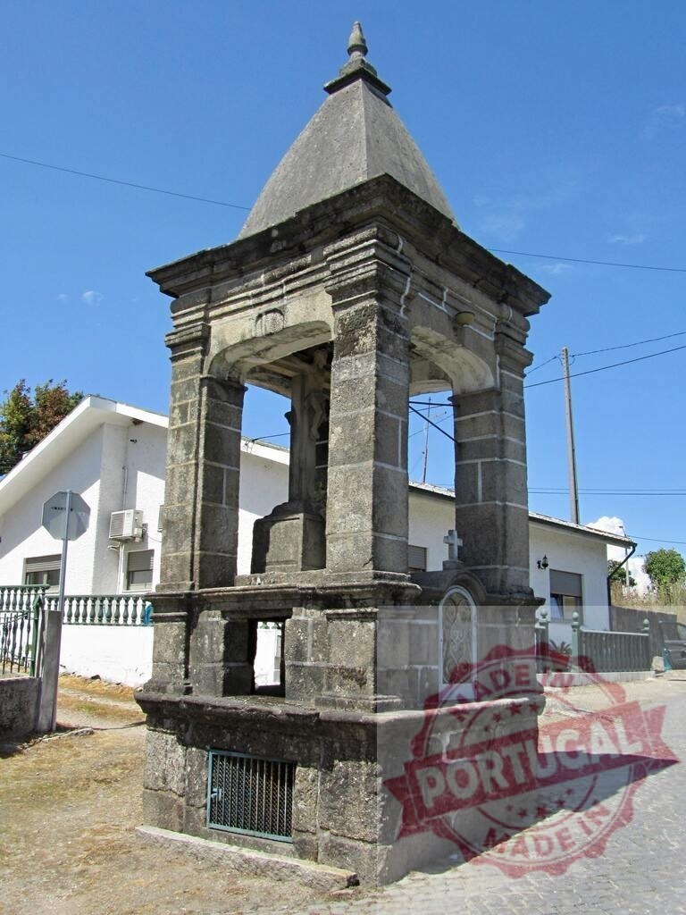 Stone shrine, cruzado, historical architecture in Portuguese village. Norte - Portugal | Stone shrine with Cruzado cross and religious imagery standing in a village setting under blue sky - Realized with Pictrs.com