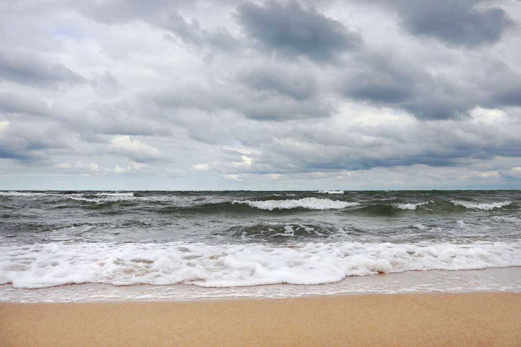 Akustikbild: Wellen und Wolken am Ostseestrand | Dieses Akustikbild zeigt einen Sandstrand an der Ostsee bei starker Bewölkung. Im Vordergrund ist der schöne Sandstrand zu sehen, der Wärme in das Wandbild bringt. Am Himmel befinden sich Wolken in vielen unterschiedlichen Grautönen. Genau wie der Himmel ist auch das Meer hellgrau bis dunkelgrau. Einige Schaumkronen auf den Wellen bringen etwas weiß ins Meer.  - Realisiert mit Pictrs.com