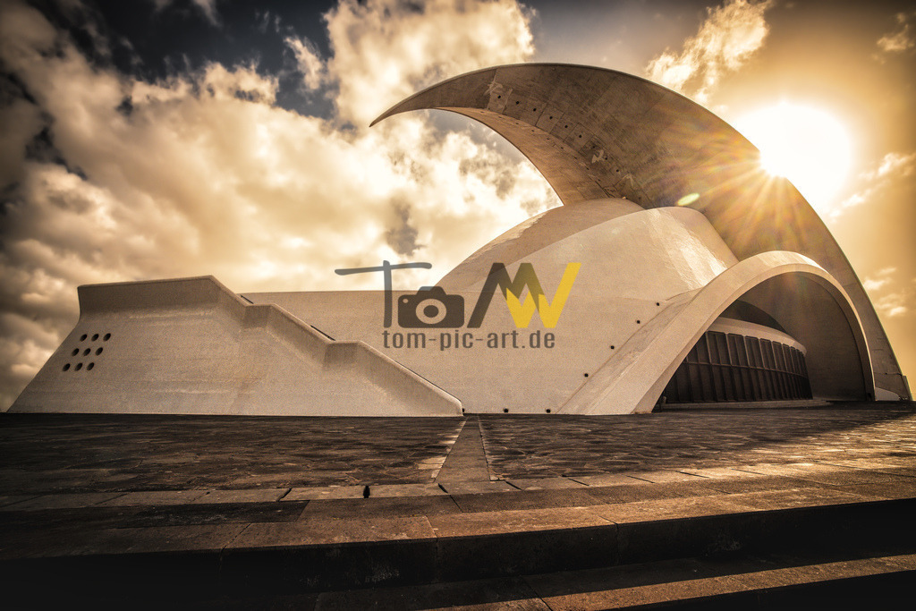 Das Auditorio de Tenerife Adán Martín in Santa Cruz de Tenerife  | Das abgebildete Gebäude ist das Auditorio de Tenerife Adán Martín. Es handelt sich um eine Kongress- und Konzerthalle in Santa Cruz de Tenerife, der Hauptstadt der Kanarischen Inseln. Das ikonische Bauwerk wurde vom bekannten spanischen Architekten Santiago Calatrava entworfen. Es ist bekannt für seine einzigartige, geschwungene Architektur, insbesondere das große "Segel" oder den Bogen über dem Hauptgebäude. Das Auditorium gilt als ein Wahrzeichen der Stadt und ist ein beliebtes Ziel für Touristen und Fotografen.  - Realisiert mit Pictrs.com