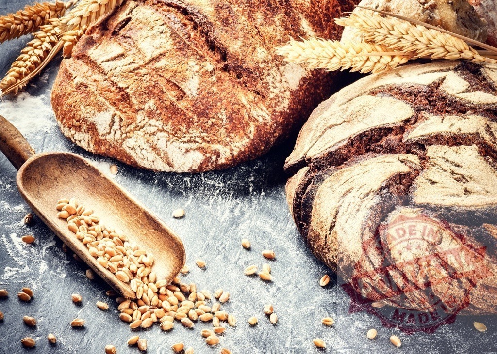 Freshly baked artisan bread with wheat grains and ears | Rustic loaves of bread, wheat ears, and grains on a dark surface with flour - Realized with Pictrs.com