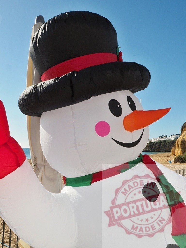 Giant inflatable snowman waving on a sunny beach | Large inflatable snowman wearing a hat and scarf waving on a beach - Realized with Pictrs.com